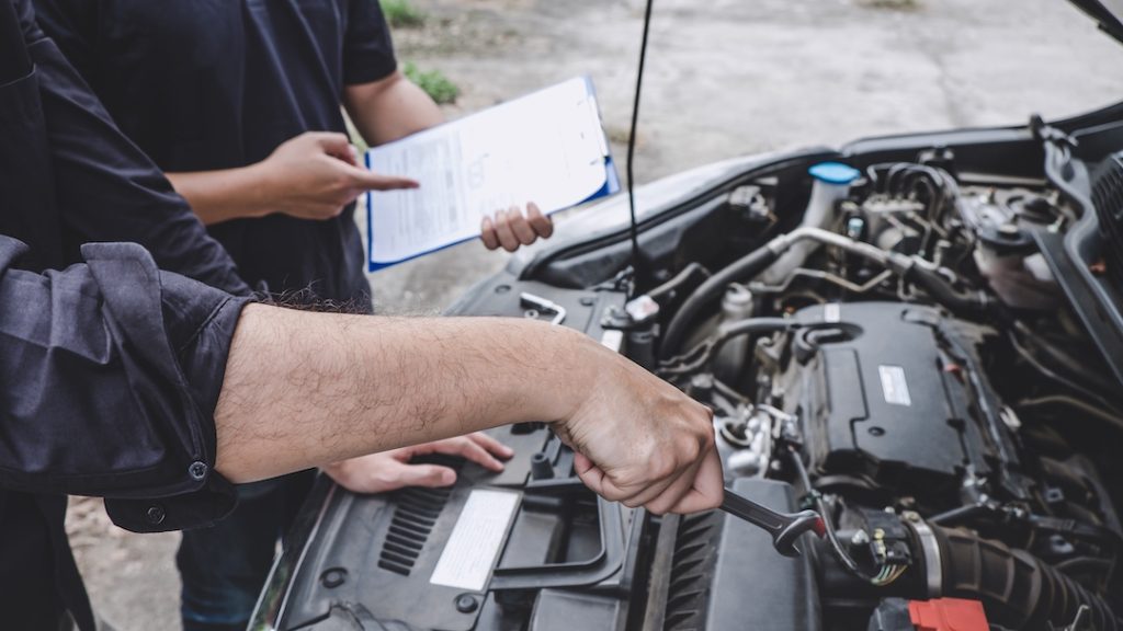 Two mechanics inspecting a vehicle engine during a WOF check