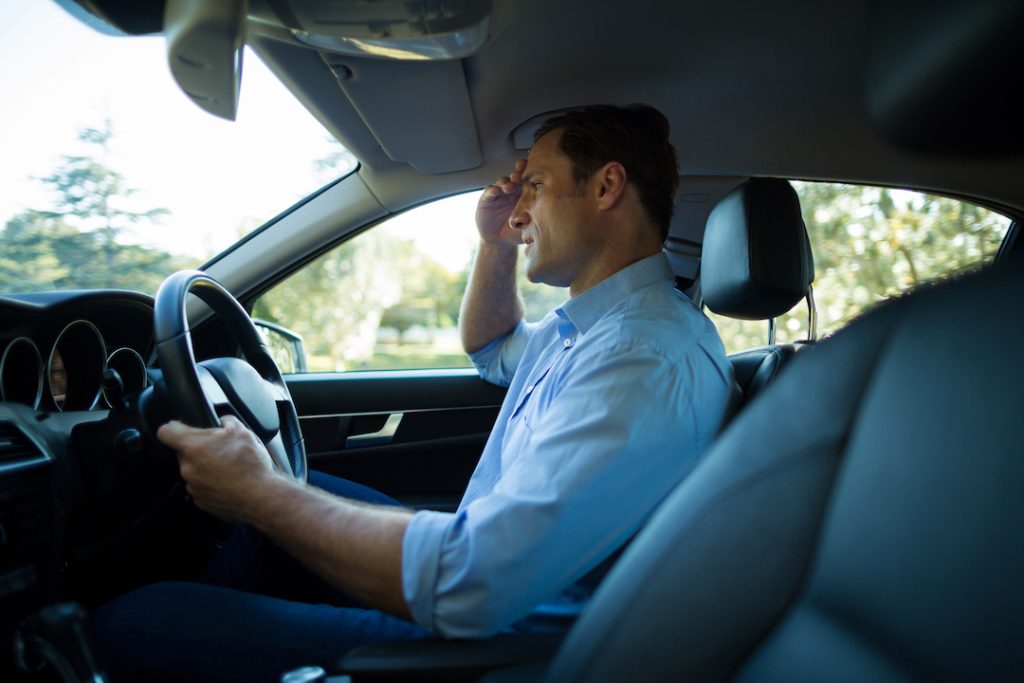 Driver looking tense while holding the steering wheel and shielding their eyes